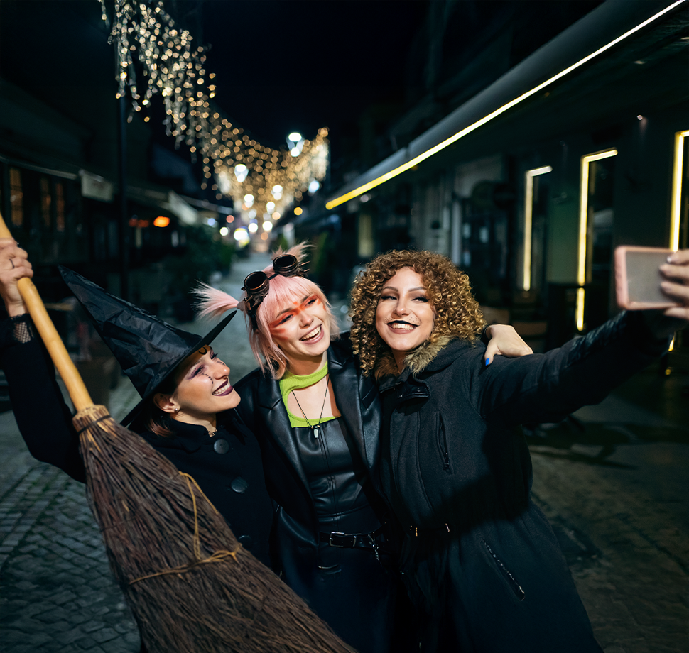 Drei verkleidete Frauen nehmen ein Halloween-Selfie mit ihrem Smartphone auf.
