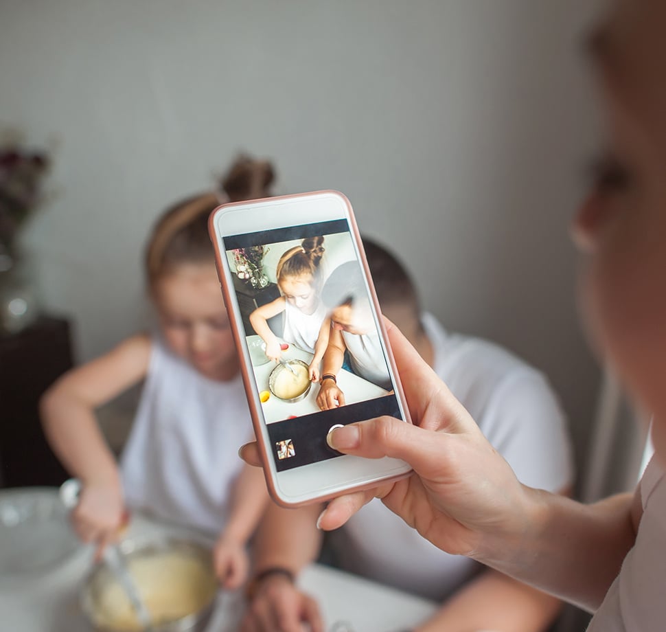 Mutter fotografiert ihre Kinder beim Backen mit dem Smartphone – perfekte Geschenkideen für Mamas zum Muttertag.