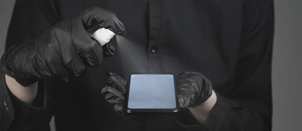 Person mit schwarzen Handschuhen reinigt Smartphone-Display mit Spray – DIY-Smartphone-Reparatur und Pflege