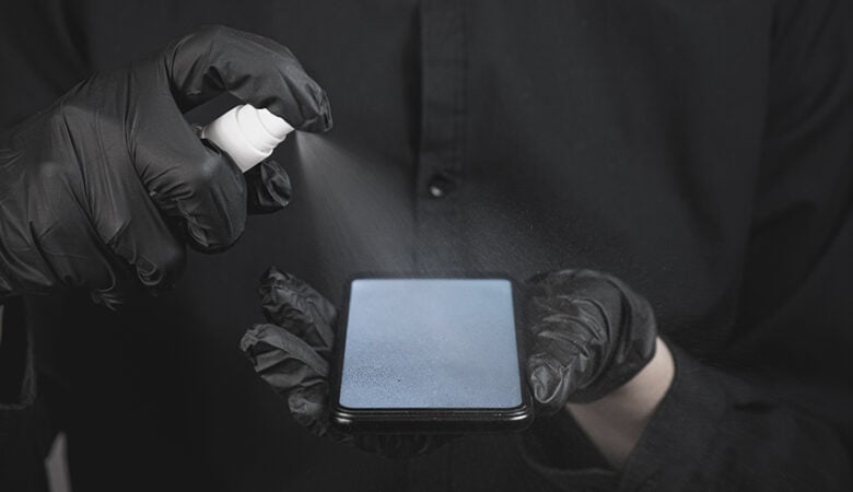Person mit schwarzen Handschuhen reinigt Smartphone-Display mit Spray – DIY-Smartphone-Reparatur und Pflege