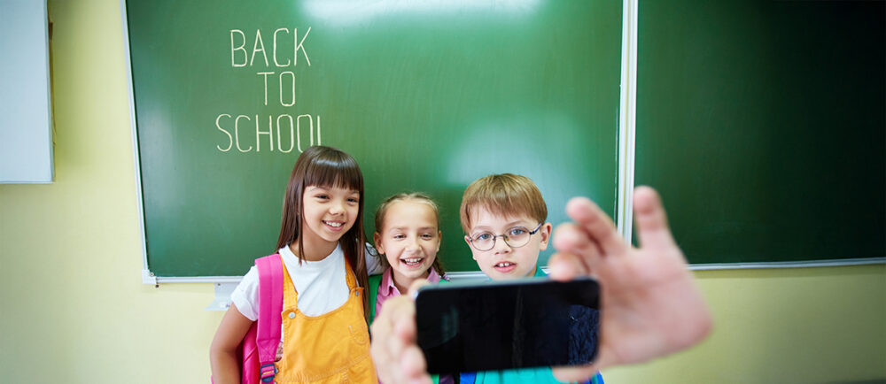 Smartphones für die Schule. Kinder vor eine Tafel mit einem Smartphone in der Hand.