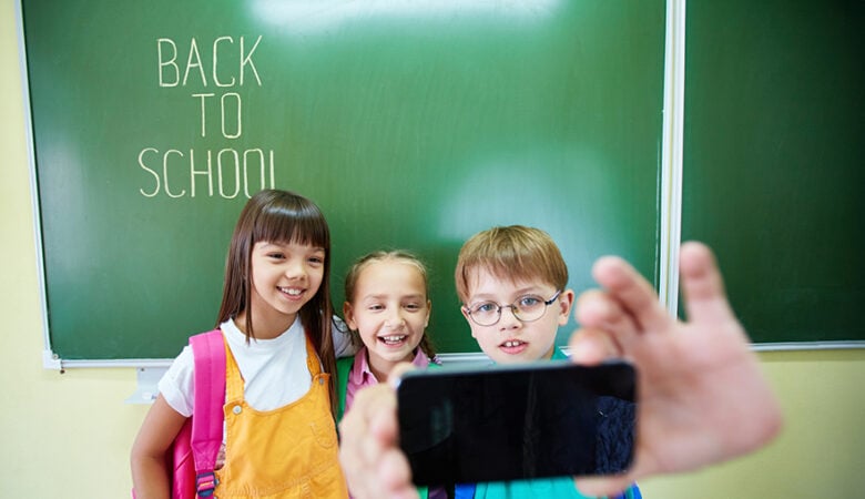 Smartphones für die Schule. Kinder vor eine Tafel mit einem Smartphone in der Hand.